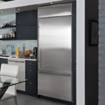 Šedá kovová lednička v interiéru černé a bílé kuchyně