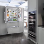 Ledusskapis virtuves interjerā gaiši pelēkā skapī