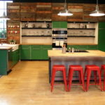 Raudonos baro kėdės ir žalios virtuvės spintelės
