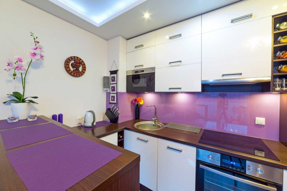 Białe szafki nad liliowym fartuchem w małej kuchni