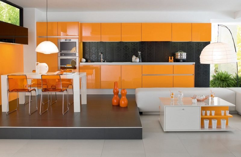 Bucătărie portocalie cu zonă de luat masa pe podium.