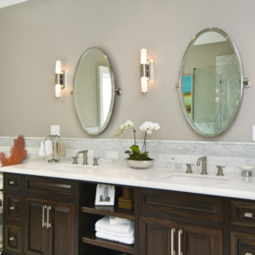 Divi ovāli spoguļi pie sienas vannas istabā
