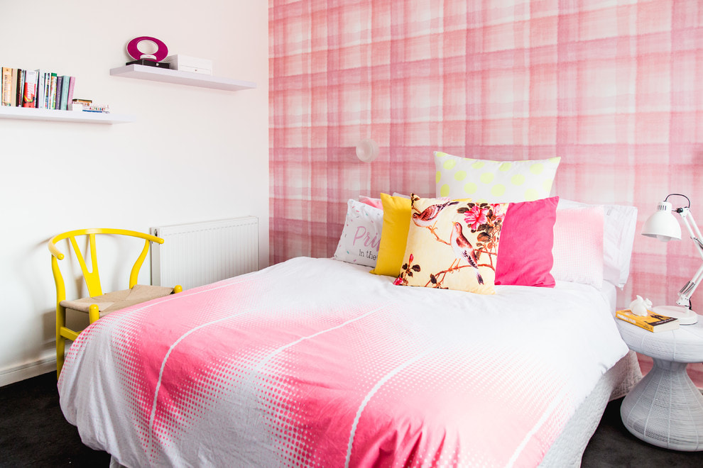 Keltainen tuoli lähellä sänkyä vaaleanpunaisella ja valkoisella peitolla