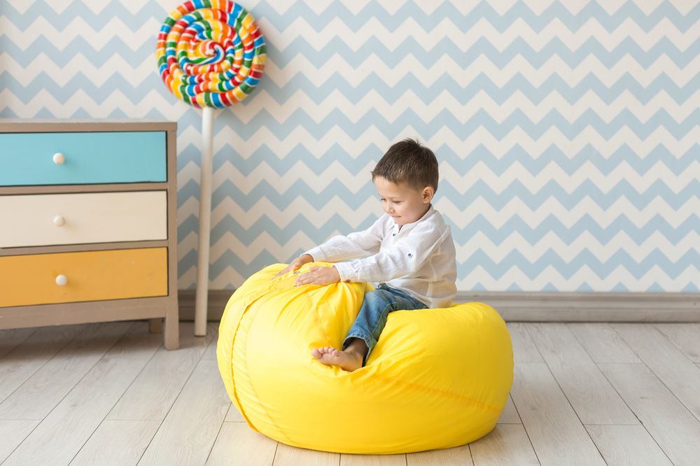 Copilul de pe un scaun cu sac de fasole galbenă în camera lui