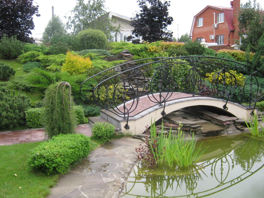 A bridge with forged railing over an artificial pond